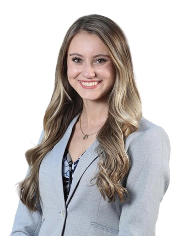 Madalyn Lyons - A smiling white woman with long wavy light brown hair. She is wearing a light blue blazer over a blue and gray floral blouse. She also has on a gold necklace.