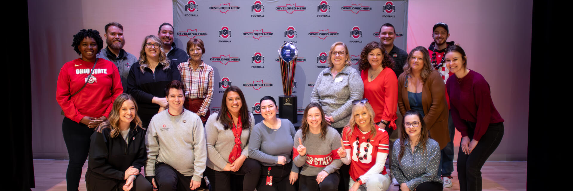 A group of SLDS staff wearing scarlet and gray, next to the national championship trophy.