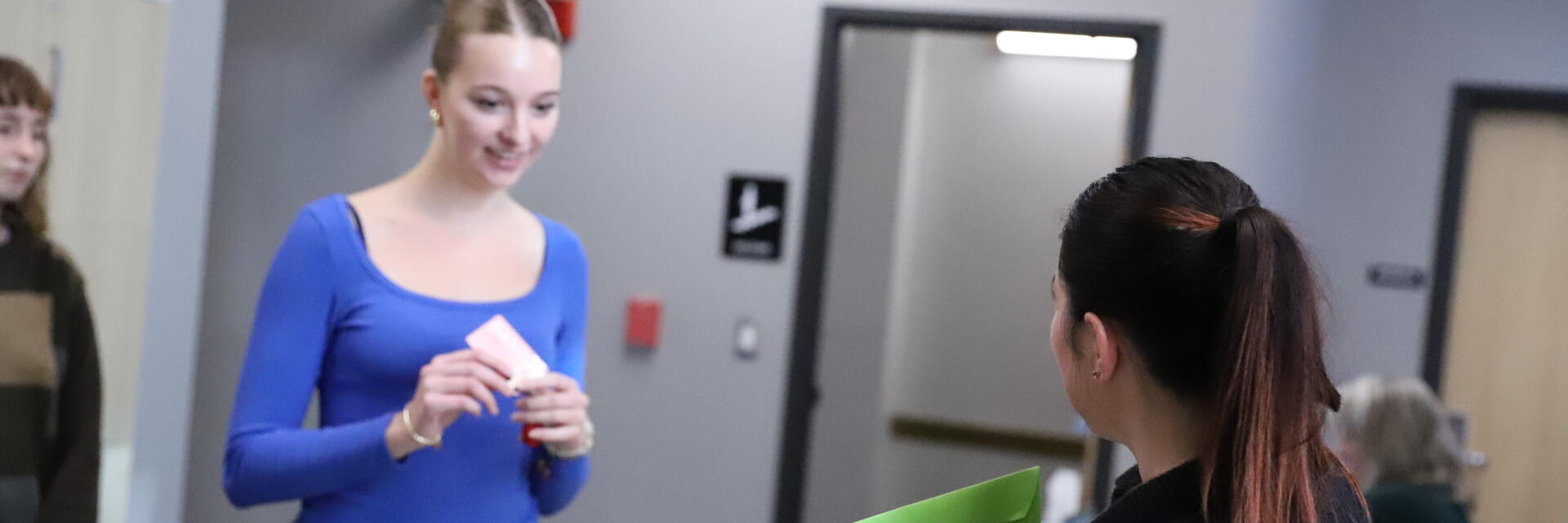 Staff member shows exam envelope to student checking in at table.