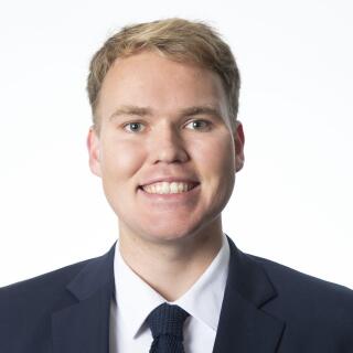 Connor Ruetz, a smiling white man with blonde hair, wearing a white shirt, blue suit coat, and tie.