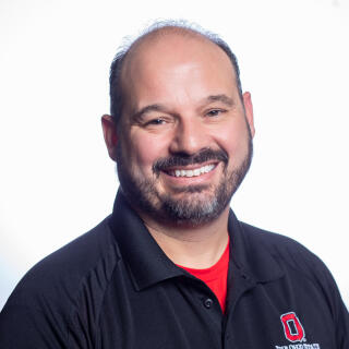 A smiling Mexican-American man wearing a black Office of Student Life polo.
