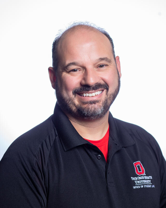 A smiling Mexican-American man wearing a black Office of Student Life polo.