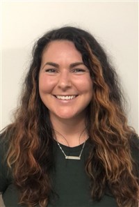 Dylan Delay, a white woman with long, wavy brown hair wearing a green t-shirt and silver necklace.