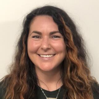 Dylan Delay, a white woman with long, wavy brown hair wearing a green t-shirt and silver necklace.