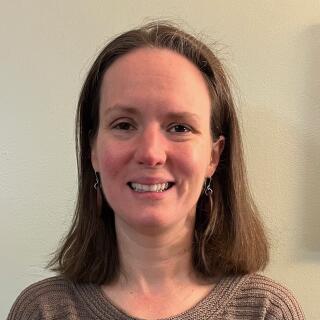 Emily Ott - a smiling white woman with long brown hair wearing a brown sweater.