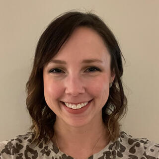 A smiling white woman with shoulder length brown hair, wearing an animal print blouse.