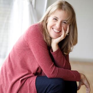 A smiling white woman with shoulder-length, brown/grey hair wearing a maroon blouse.