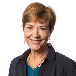 A white woman with short reddish hair, wearing a turquoise top under a navy blue shirt.
