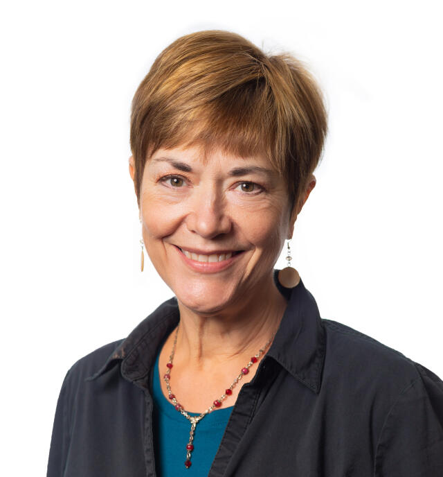 A white woman with short reddish hair, wearing a turquoise top under a navy blue shirt.
