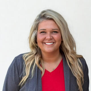 Lauren Pullins- A smiling white woman with long blonde hair, wearing a red dress with a gray blazer