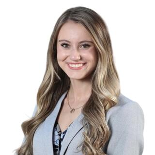 A white woman with light brown hair, wearing a blazer, floral blouse, and necklace.