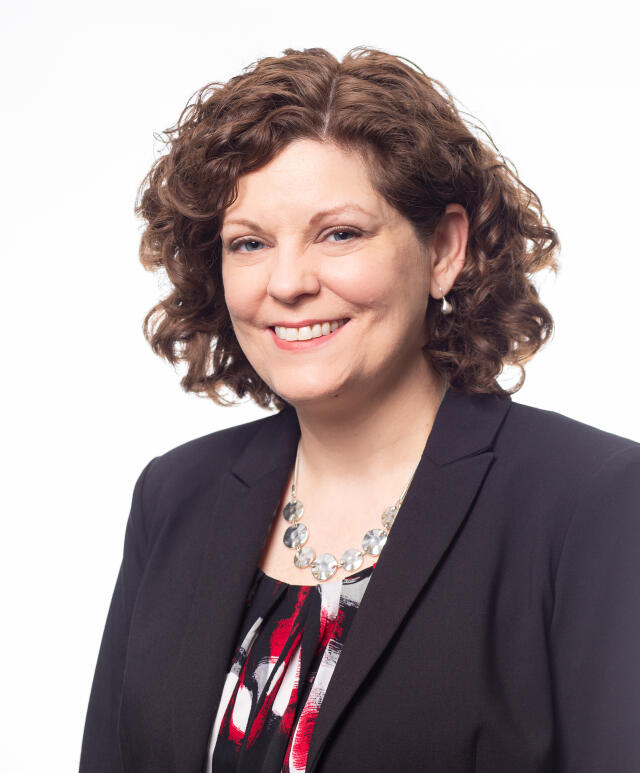 Dr. Cheryl Lyons - A white woman with chin length curly brown hair, wearing a blazer and blouse.