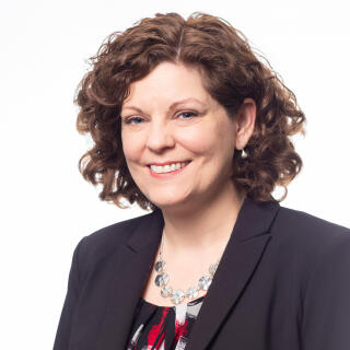 Dr. Cheryl Lyons - A white woman with chin length curly brown hair, wearing a blazer and blouse.