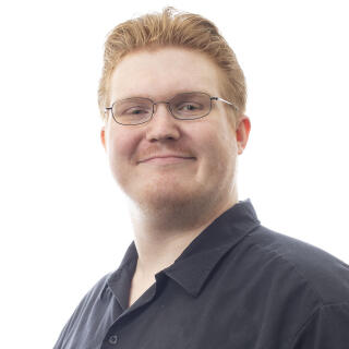 A white man with short, red hair and glasses, wearing a black button-down shirt.