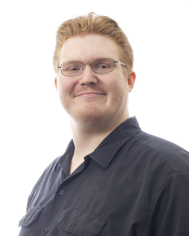 A white man with short, red hair and glasses, wearing a black button-down shirt.
