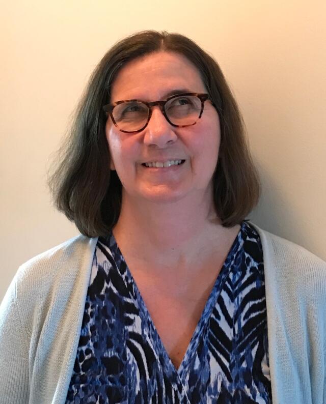 Michelle Salomone - a white woman with brown hair wearing a blouse, a sweater, and glasses.