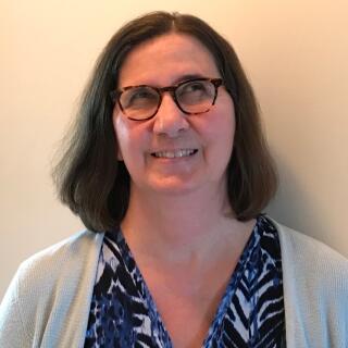 Michelle Salomone - a white woman with brown hair wearing a blouse, a sweater, and glasses.