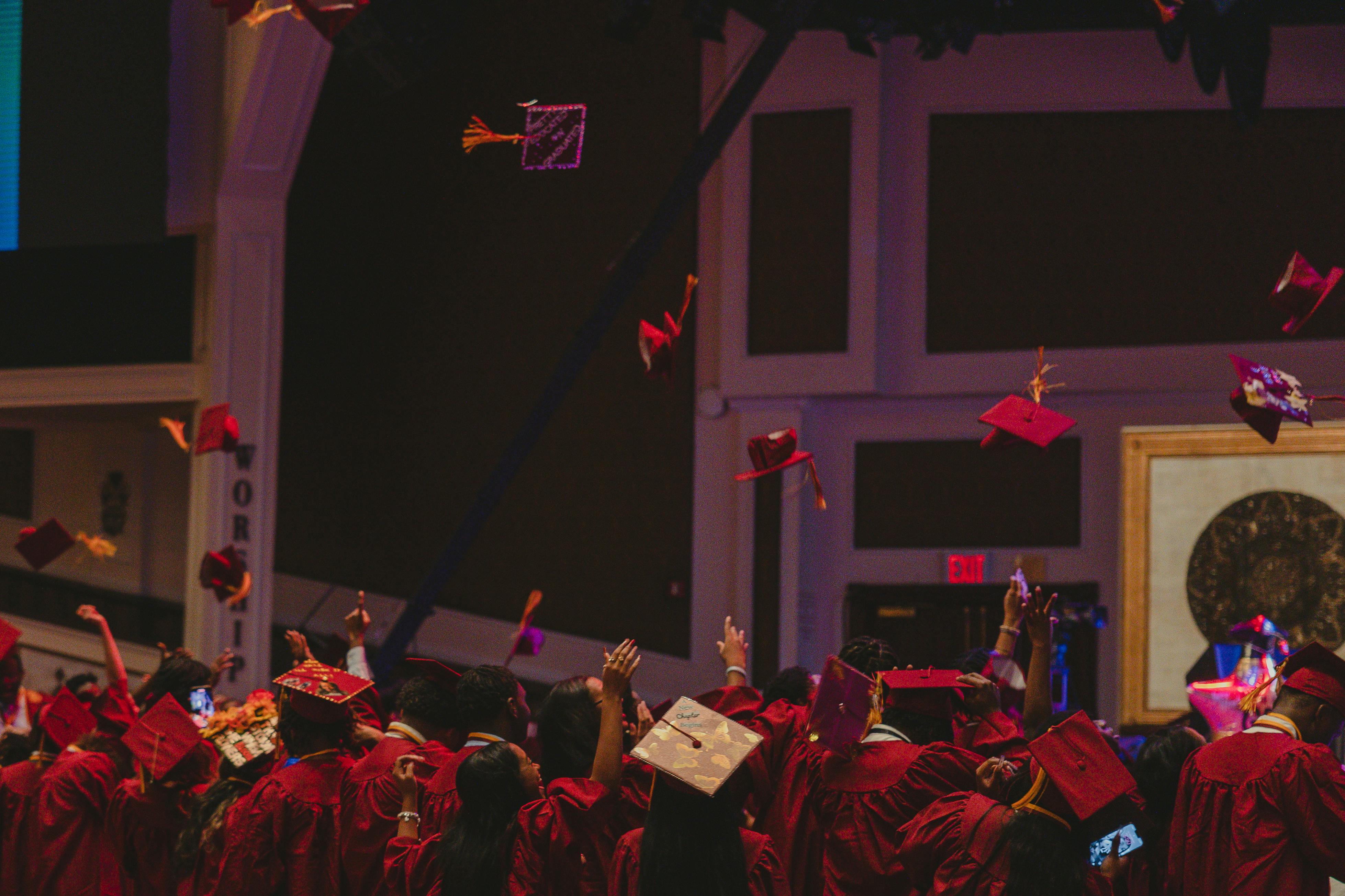 High School Graduation Mortarboard Toss Scene shown from back of auditorium - grads in red gowns