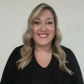 Sam Dible, a smiling white woman with wavy blonde hair, wearing a black top and blazer.