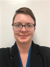 Sara Yurkovic, a white woman with short brown hair and glasses wearing a blouse and blazer.
