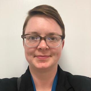 Sara Yurkovic, a white woman with short brown hair and glasses wearing a blouse and blazer.