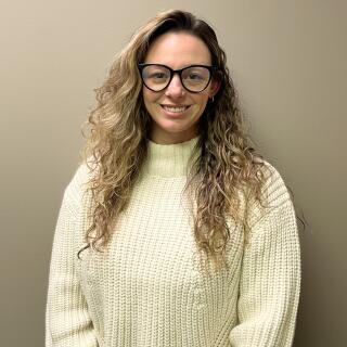 A white woman with long curly light brown hair, wearing glasses and a turtleneck.