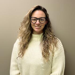 Shelby Koehler, a white woman with long curly light brown hair, wearing glasses and a turtleneck.
