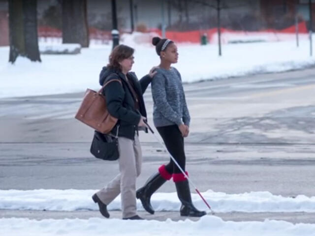 Blind student with aide walking across street
