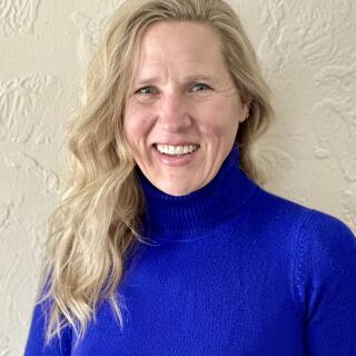 Tiffany Hedges, a white woman with wavy blond hair, parted on the side, wearing a blue turtleneck.